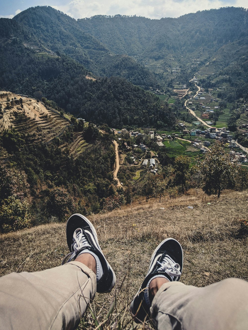 person in brown pants and black and white sneakers sitting on brown rock during daytime