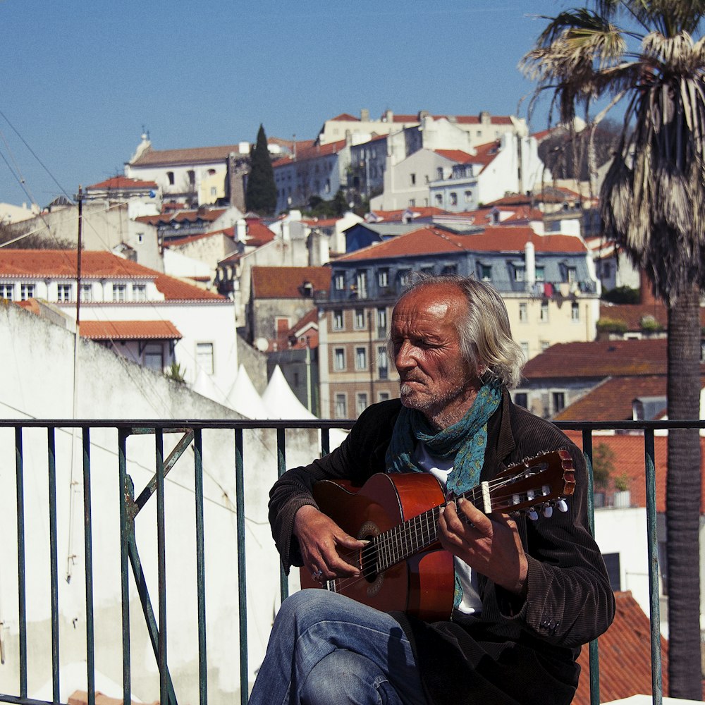 a man sitting on a balcony playing a guitar