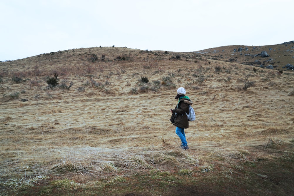 person in blue jacket walking on brown field during daytime