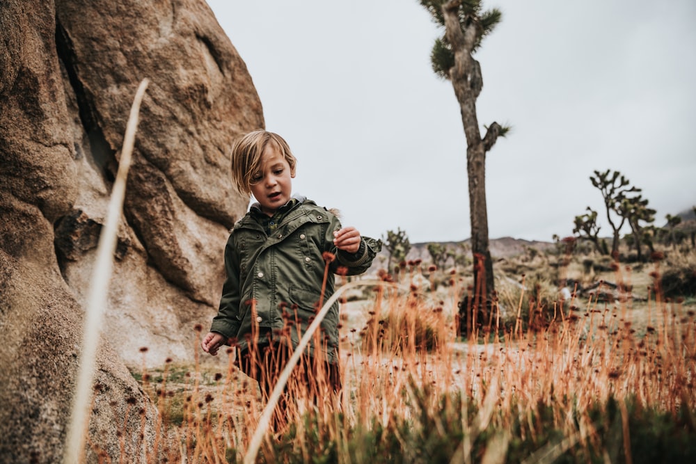 boy in green jacket holding stick near brown rock during daytime