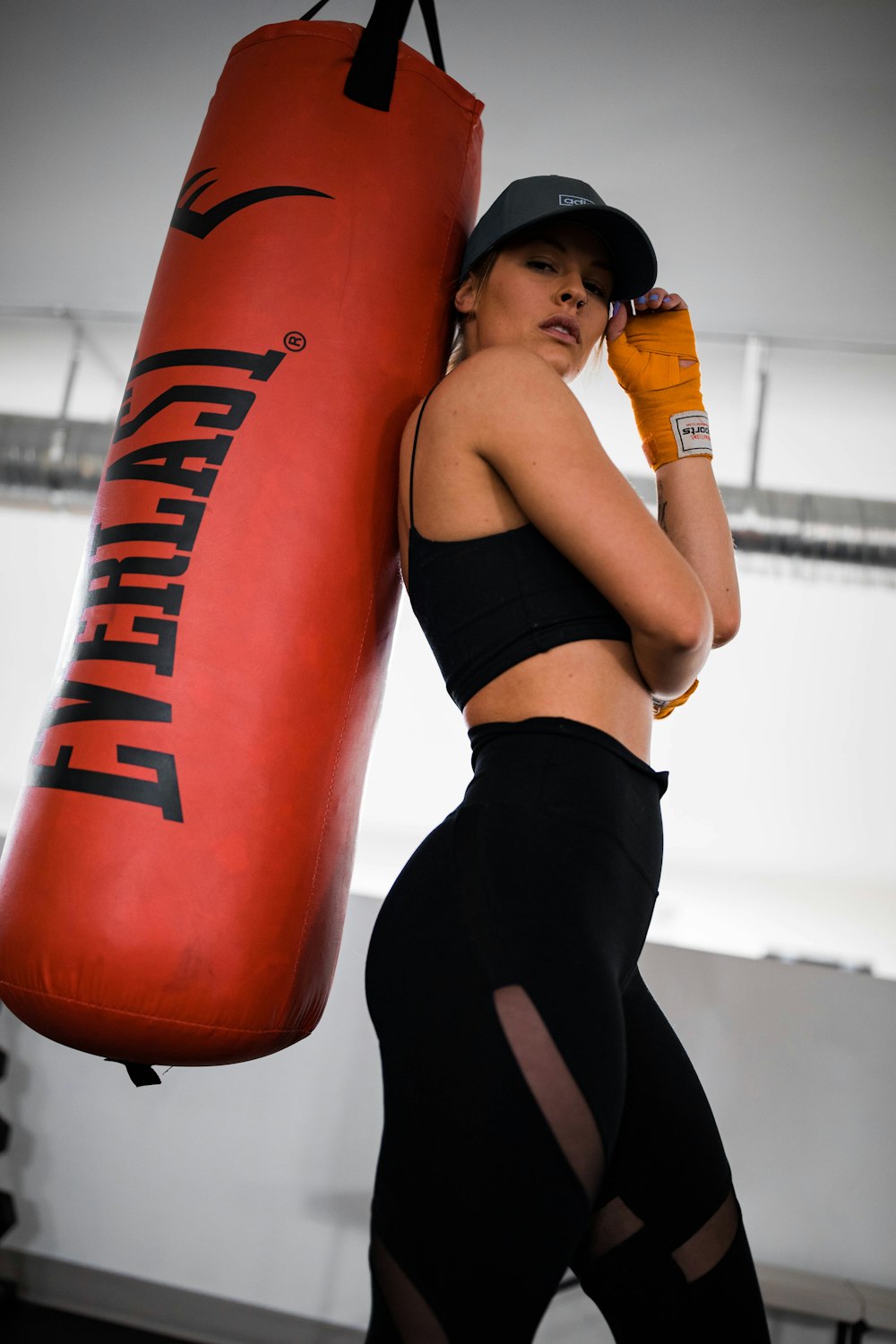 woman in black sports bra and black shorts leaning on orange and black boxing ring