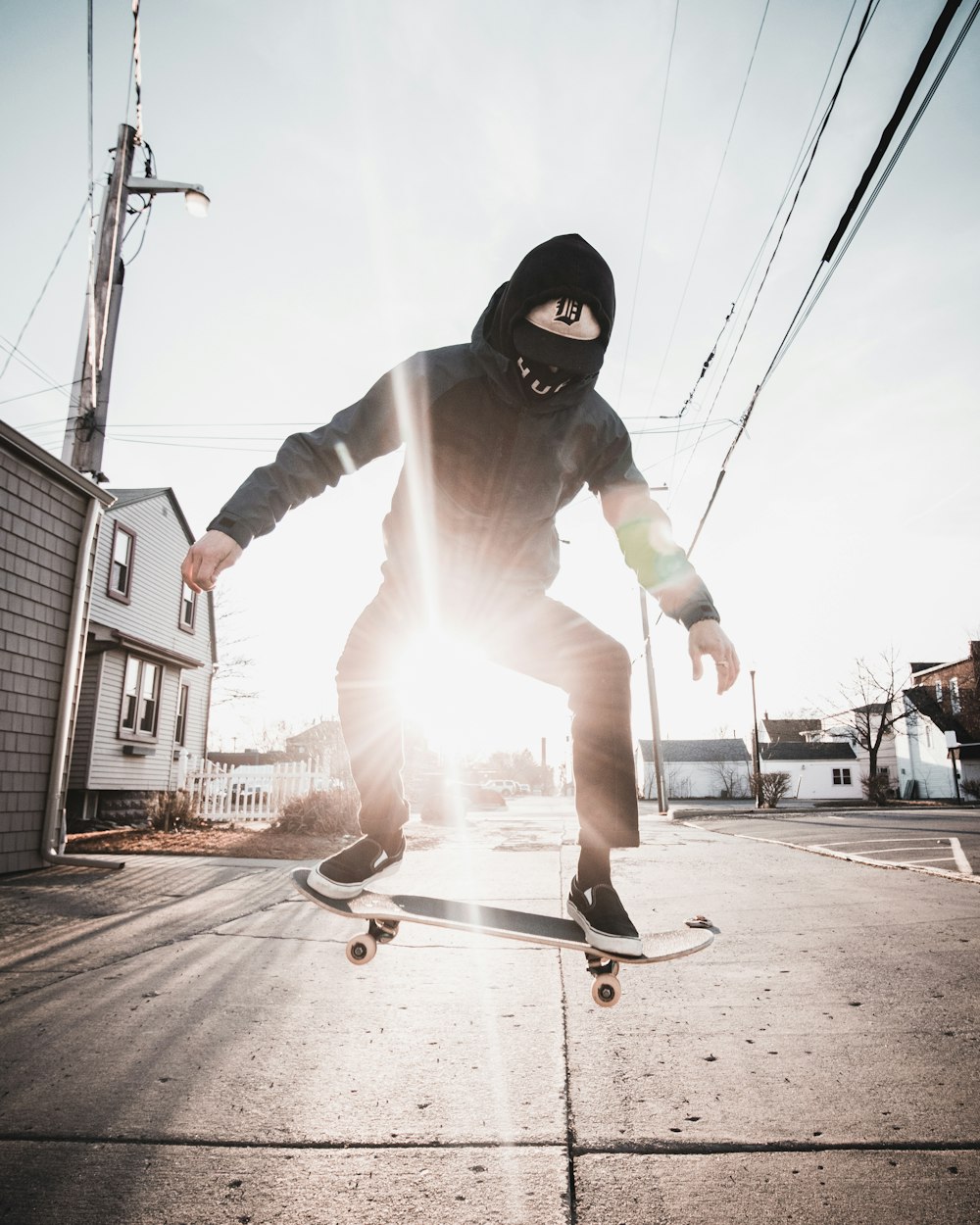 uomo in felpa con cappuccio nera e pantaloni bianchi che cavalcano lo skateboard durante il giorno