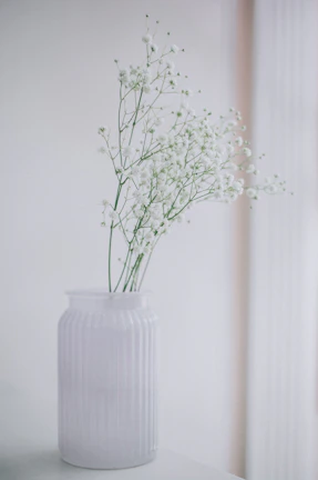 Minimalist floral design in a neutral-toned vase placed on a cozy living room side table.