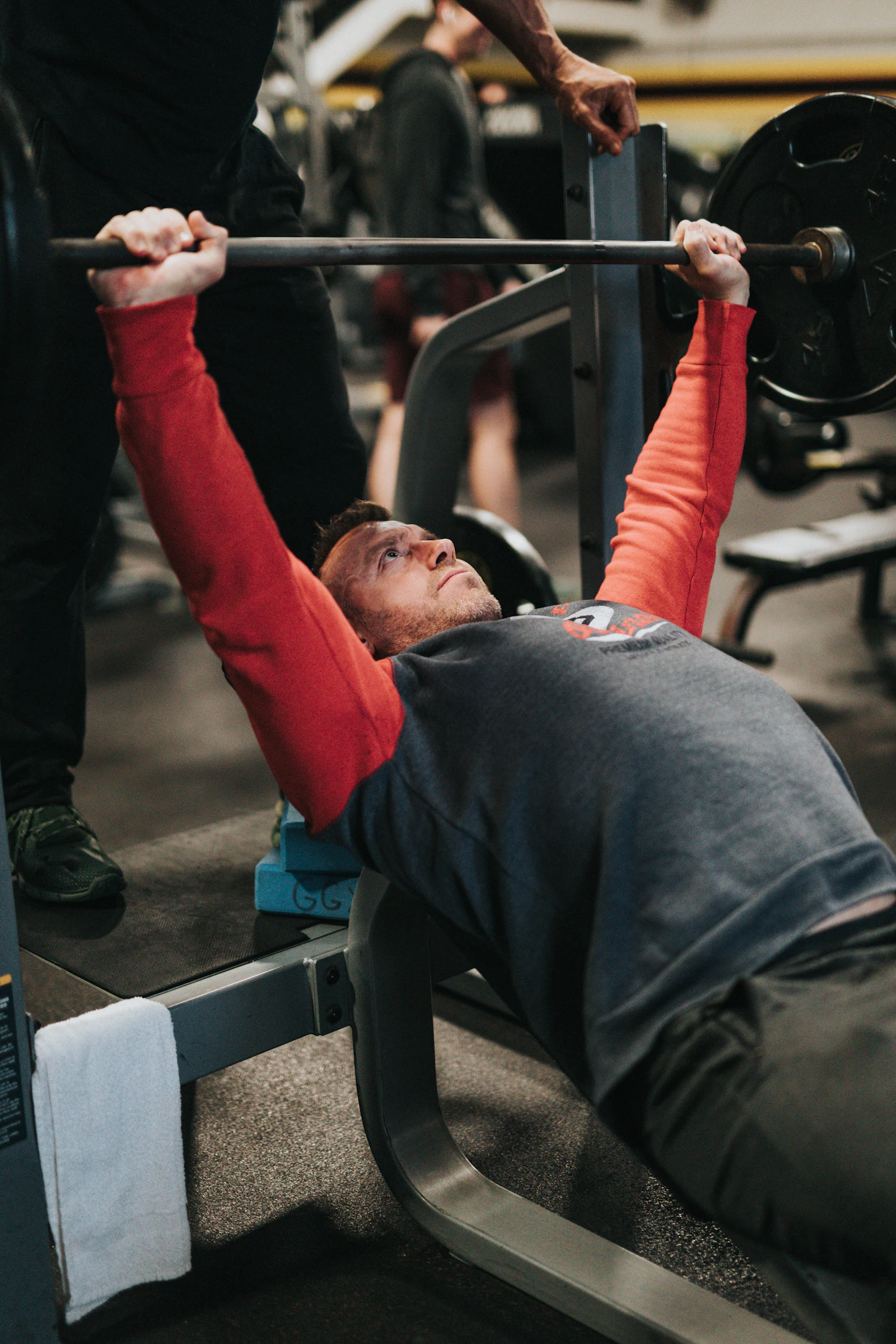 Bearded man mid bench press with spotter — workout performance