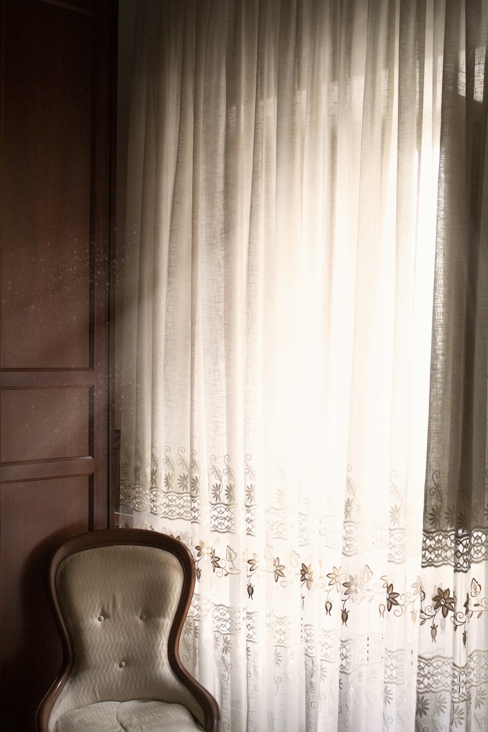 white floral window curtain near brown wooden chair