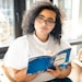 woman in white and black polka dot shirt holding blue and white book