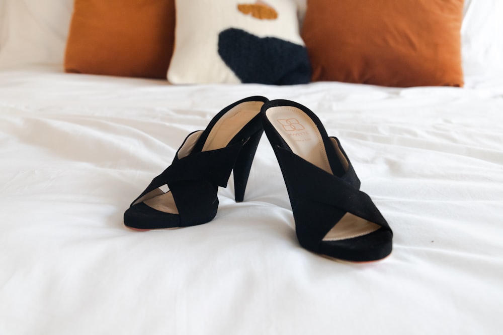black leather peep toe heeled sandals on white bed