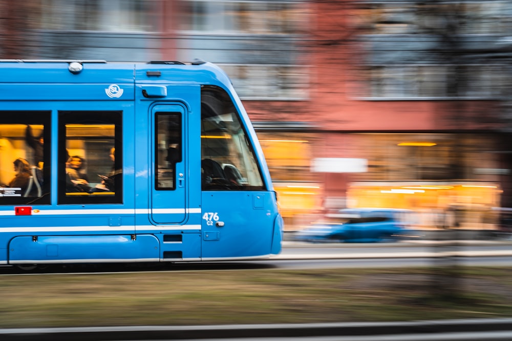 a blue train traveling down a street next to tall buildings