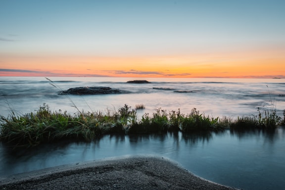 A serene coastal landscape with gentle waves lapping against the shore at sunset.