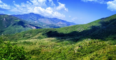 green grass field and mountains under blue sky during daytime