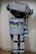 A humanoid robot costume with a metallic gray and blue color scheme, boxy limbs, and a large rectangular torso. The robot has a large head with circular antenna on top and large, round blue eyes. The front of the torso features the text 'Plug'n SAVE' in bold letters.