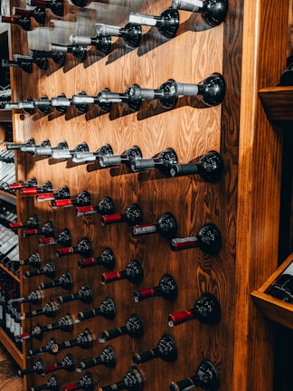 A wooden wall-mounted wine rack displays numerous bottles stored horizontally, each held securely by metal holders. The warm tones of the wood contrast with the dark colors of the wine bottles, creating an elegant and orderly arrangement.