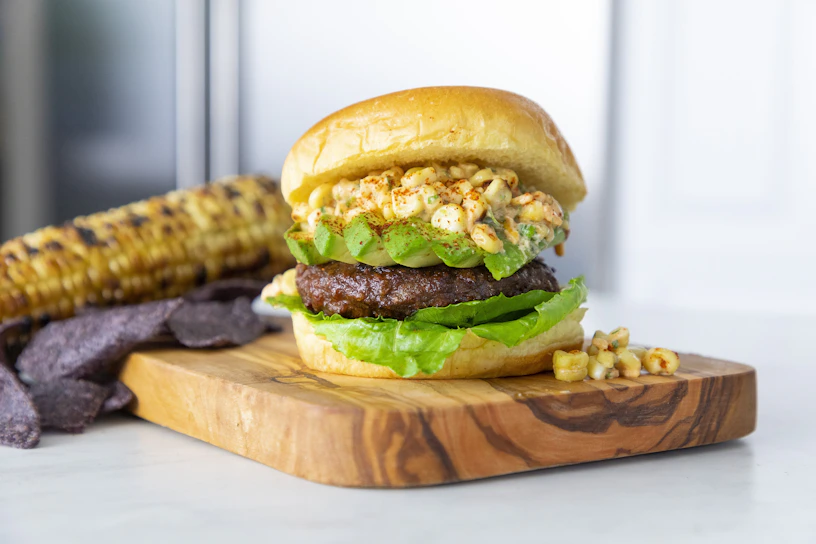 Colorful gourmet Mexican fusion burger topped with fresh avocado slices and spicy chipotle sauce on a rustic wooden board.