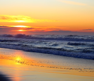 A vibrant sunset over the ocean, casting warm hues on the beach.