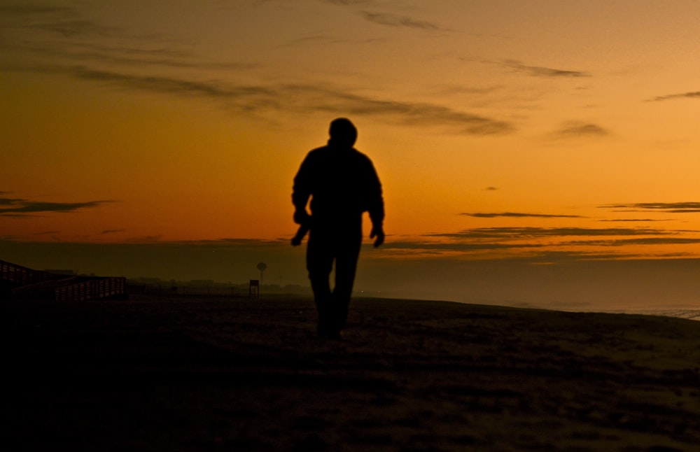 silhouette di uomo in piedi sul campo durante il tramonto