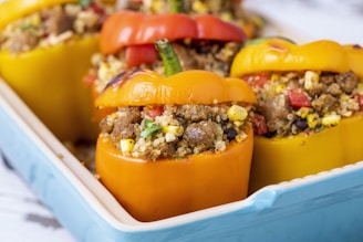 Stuffed bell peppers filled with a mixture of quinoa, ground meat, corn, black beans, and diced vegetables are arranged in a blue baking dish. The peppers are vibrant in color, featuring red, yellow, and orange hues.