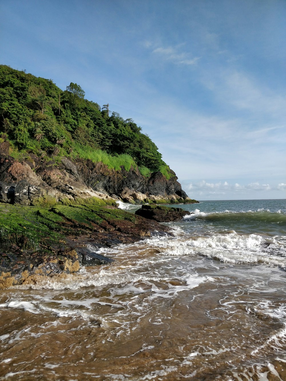 green and brown mountain beside sea under blue sky during daytime