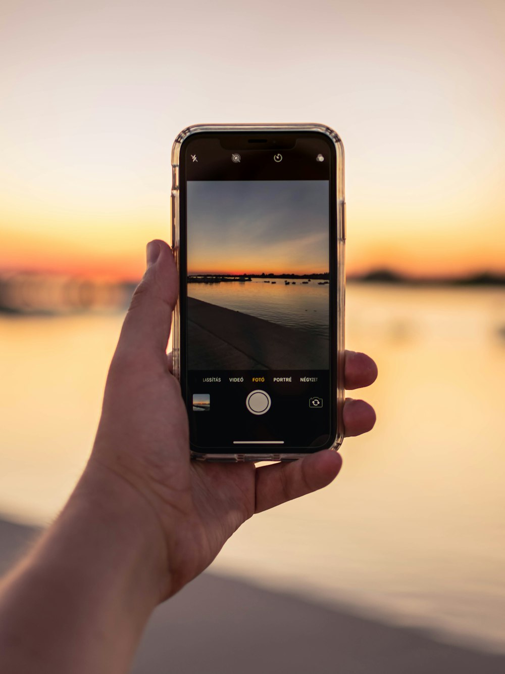 person holding iphone taking photo of sunset