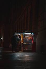 man in black jacket and black pants standing beside red and white food cart
