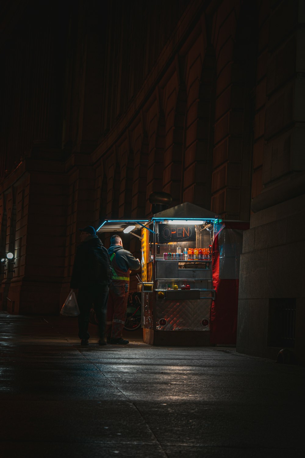man in black jacket and black pants standing beside red and white food cart