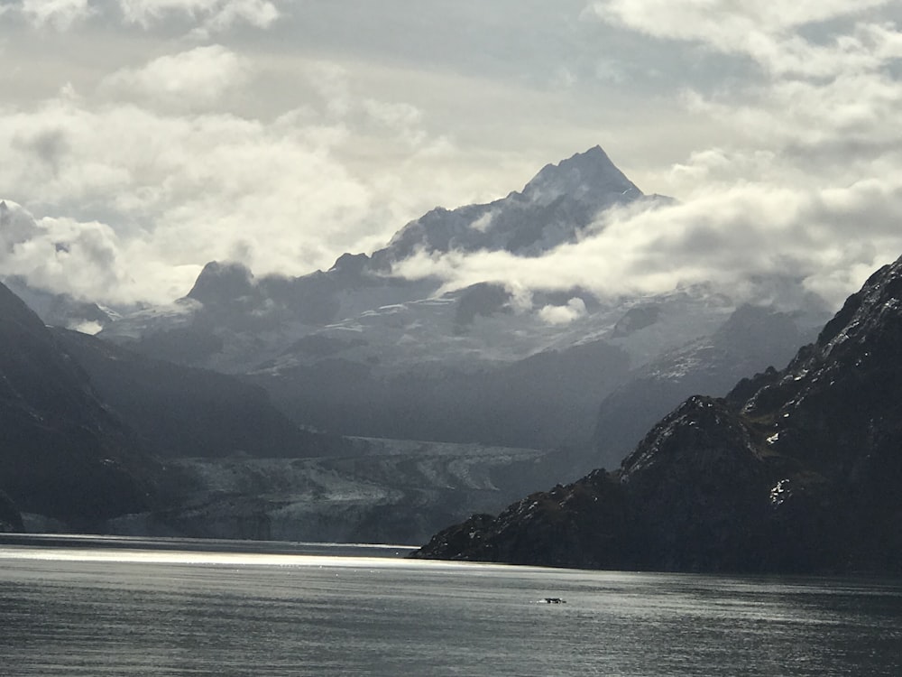 body of water near mountain under white clouds during daytime