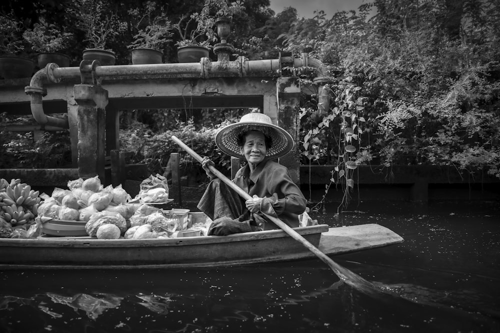 grayscale photo of man in hat riding boat