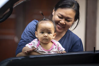 A warm, candid photo of a smiling mother using the infantocare app on her phone while holding her happy toddler.