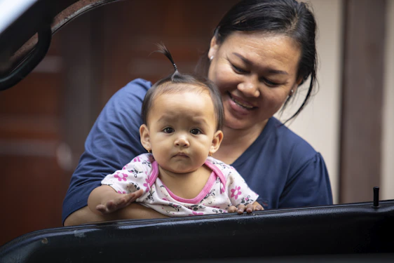 A warm, candid photo of a smiling mother using the infantocare app on her phone while holding her happy toddler.