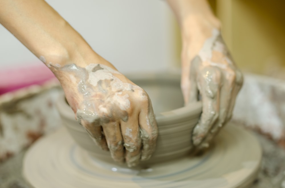 person making clay pot on brown wooden round table