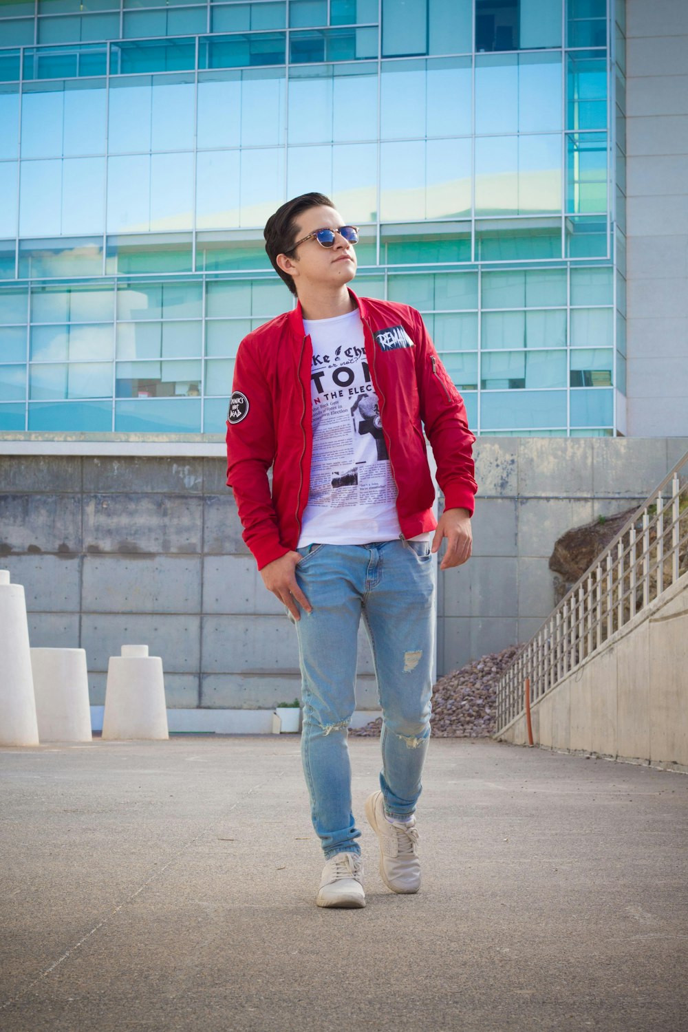 man in red and white jacket and blue denim jeans standing on gray concrete floor during