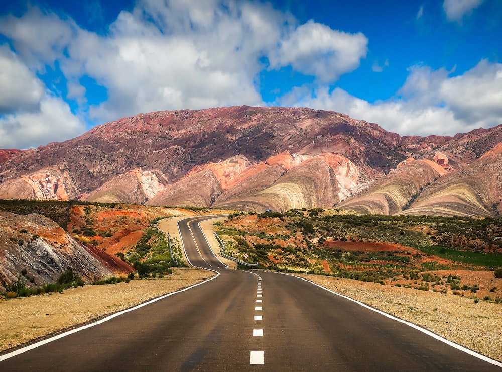 gray concrete road near brown mountain under blue sky during daytime