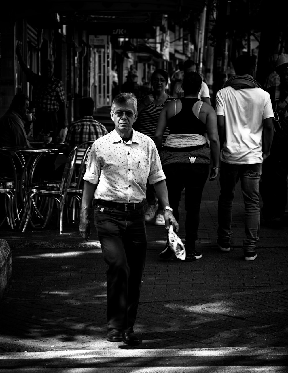 grayscale photo of man in dress shirt and pants standing on sidewalk