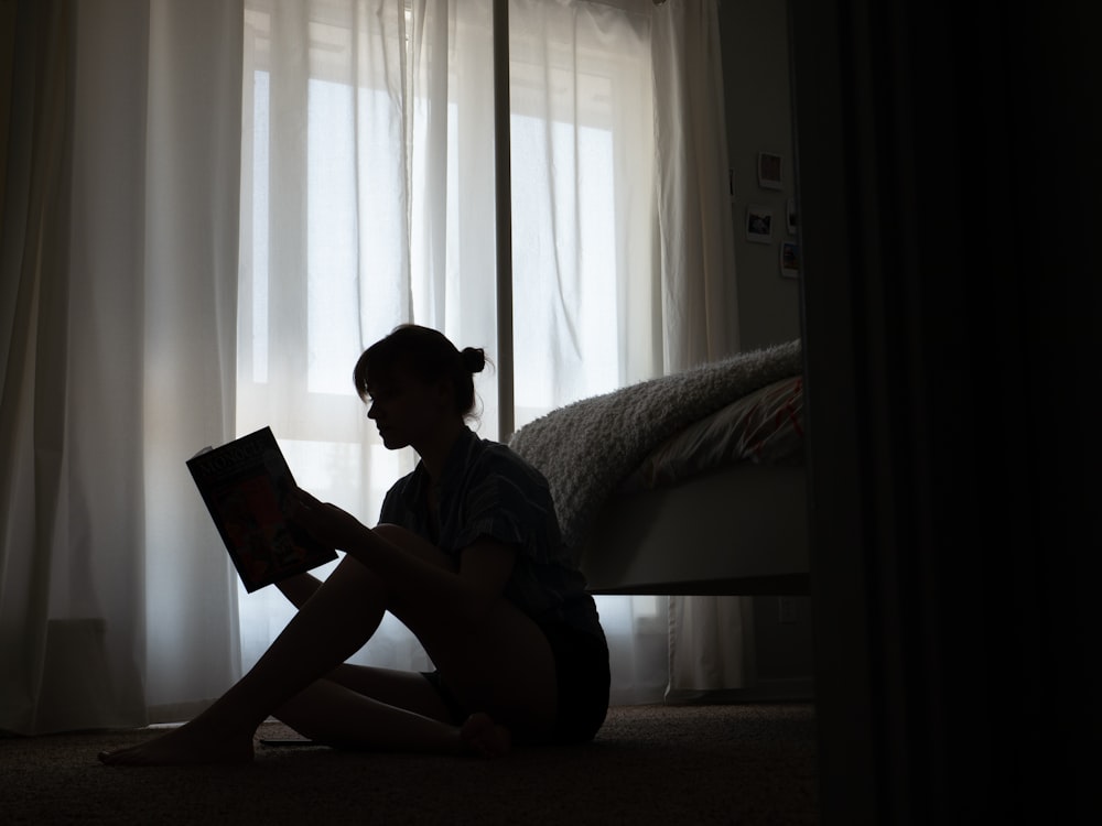 man in blue t-shirt sitting on bed reading book