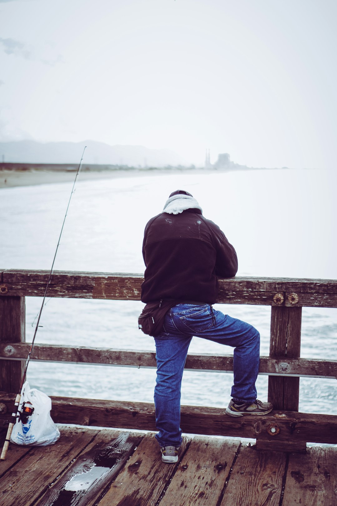 man in blue denim jeans and black jacket standing on wooden fence during daytime