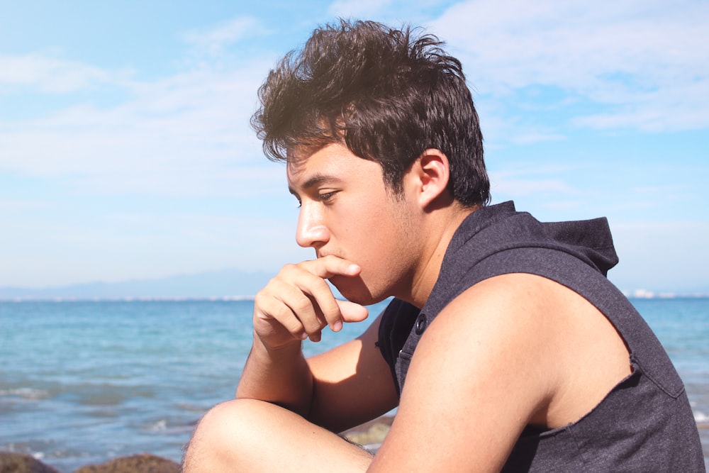 man in gray tank top sitting on beach during daytime