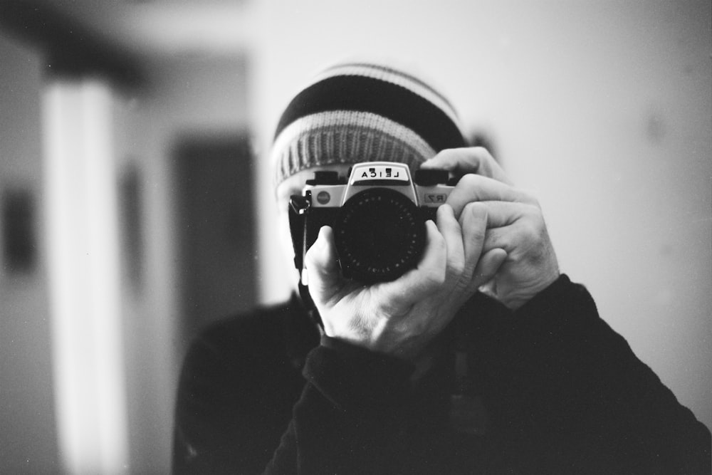Foto in scala di grigi di una persona che tiene la macchina fotografica