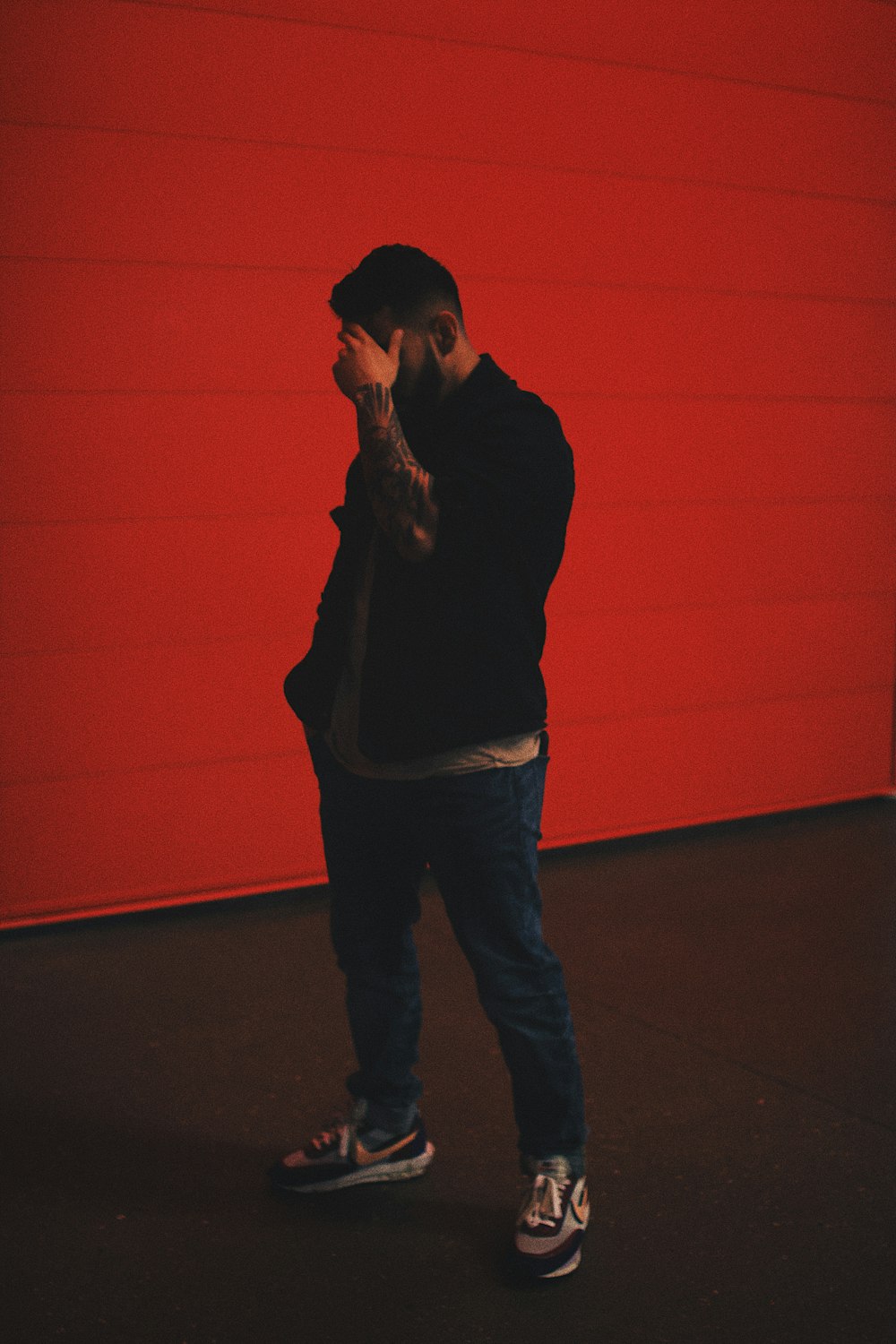 man in black long sleeve shirt and blue denim jeans standing beside orange wall