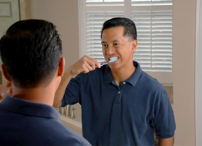 A smiling person rinsing their mouth with Lumident mouthwash in a bright bathroom.