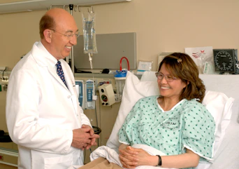 A doctor in a white coat talking to a patient in a hospital bed
