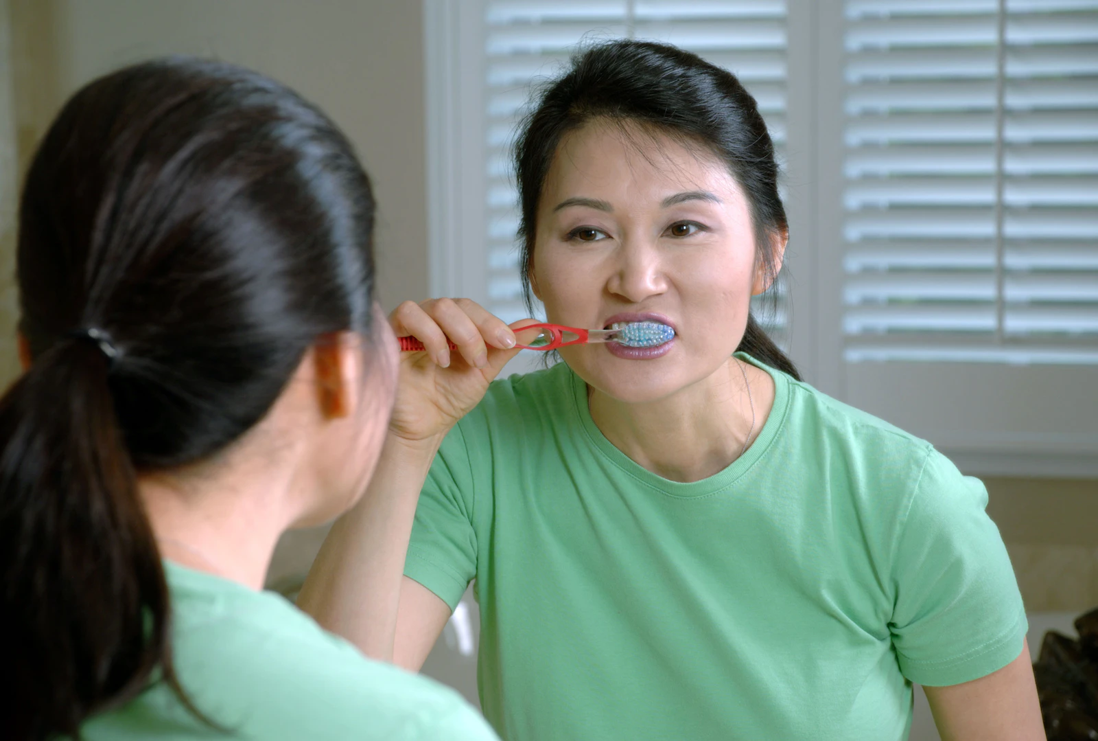 Woman brushing her teeth while looking in a mirror