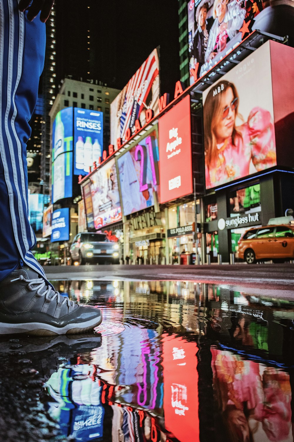 person in blue pants and black nike sneakers standing on sidewalk during night time