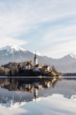 brown and white concrete building near body of water and mountain under white clouds and blue