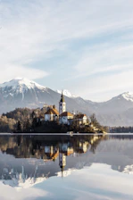 brown and white concrete building near body of water and mountain under white clouds and blue