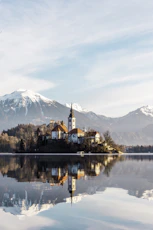 brown and white concrete building near body of water and mountain under white clouds and blue