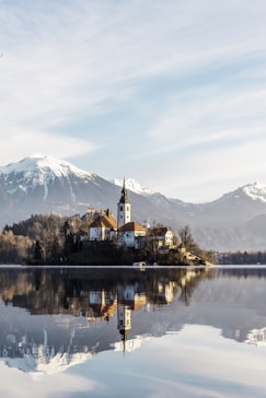 brown and white concrete building near body of water and mountain under white clouds and blue