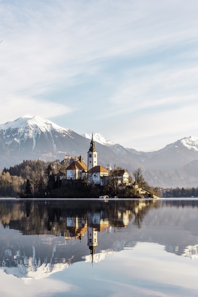 brown and white concrete building near body of water and mountain under white clouds and blue
