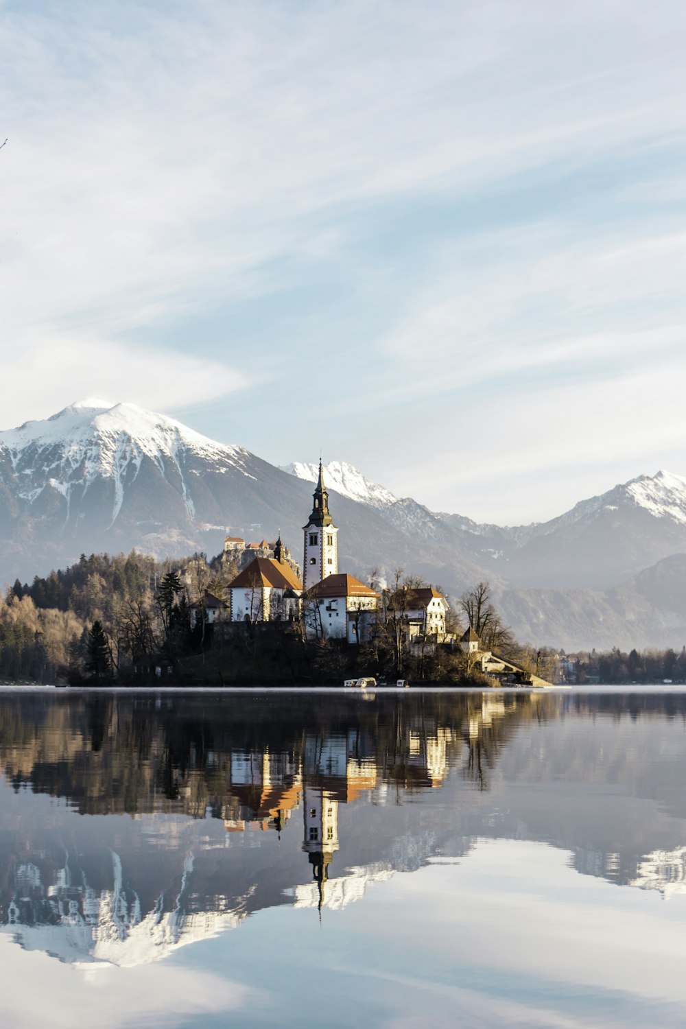 edificio in cemento marrone e bianco vicino allo specchio d'acqua e alla montagna sotto nuvole bianche e blu