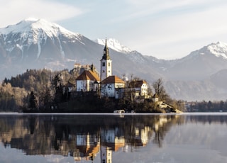 brown and white concrete building near body of water and mountain under white clouds and blue