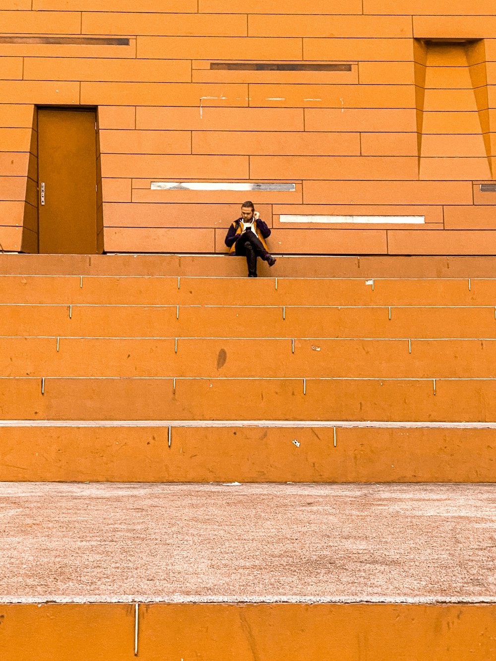 man in black jacket and pants leaning on brown brick wall during daytime