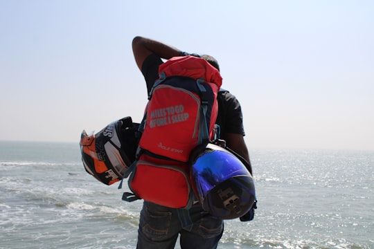 man in red and black backpack and blue denim jeans carrying red and black backpack in Diu India